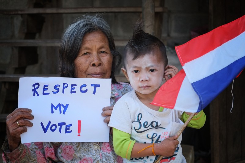 An elderly woman holds a sign that reads 'Respect My Vote' as she poses with her grandchild who holds a Thai national flag. Photo by Matthew Richards, Copyright @Demotix (1/15/2014)