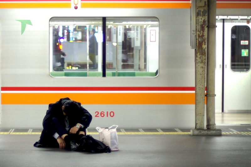 A frazzled salaryman doubled over on the floor of a train platform.